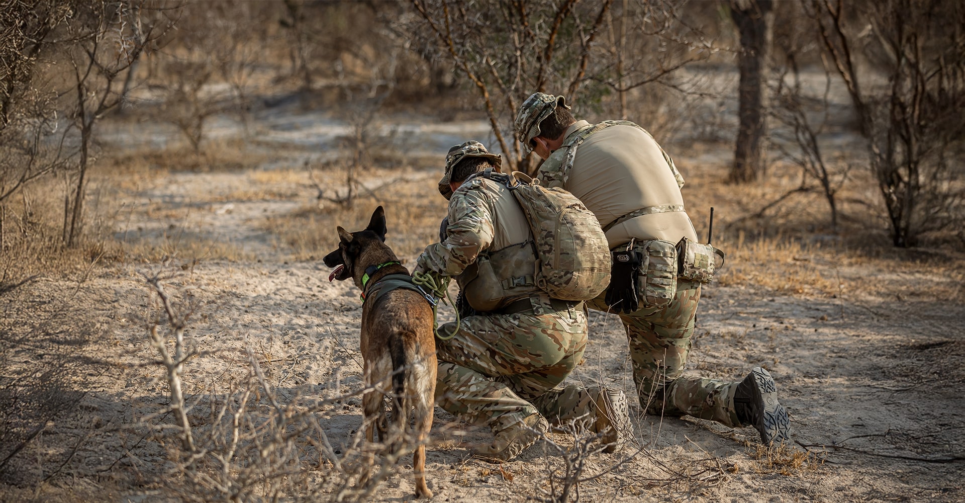 Two operators kneeling on Africa’s rugged terrain, searching for tracks identified by the K9.