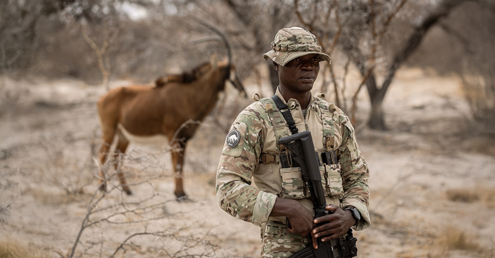 A park ranger posing in the foreground with an impala visible in the background.