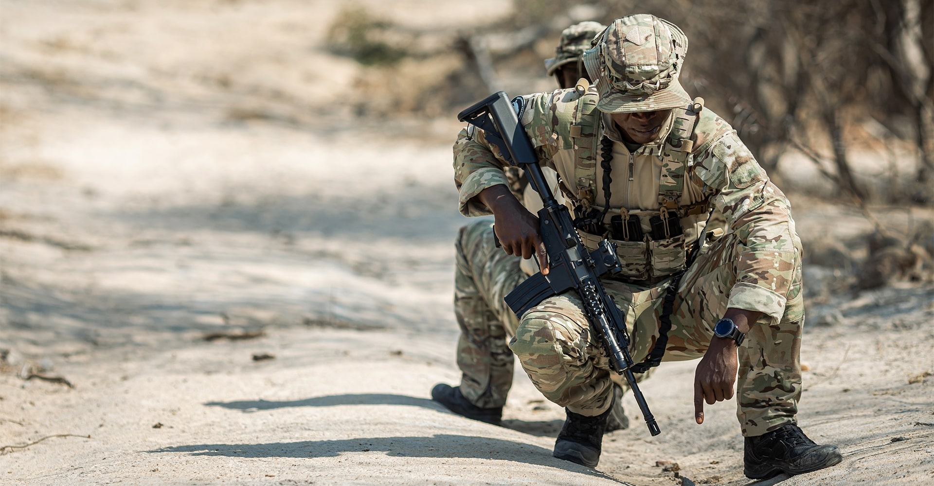 Two park rangers crouching to examine tracks in the sandy terrain.