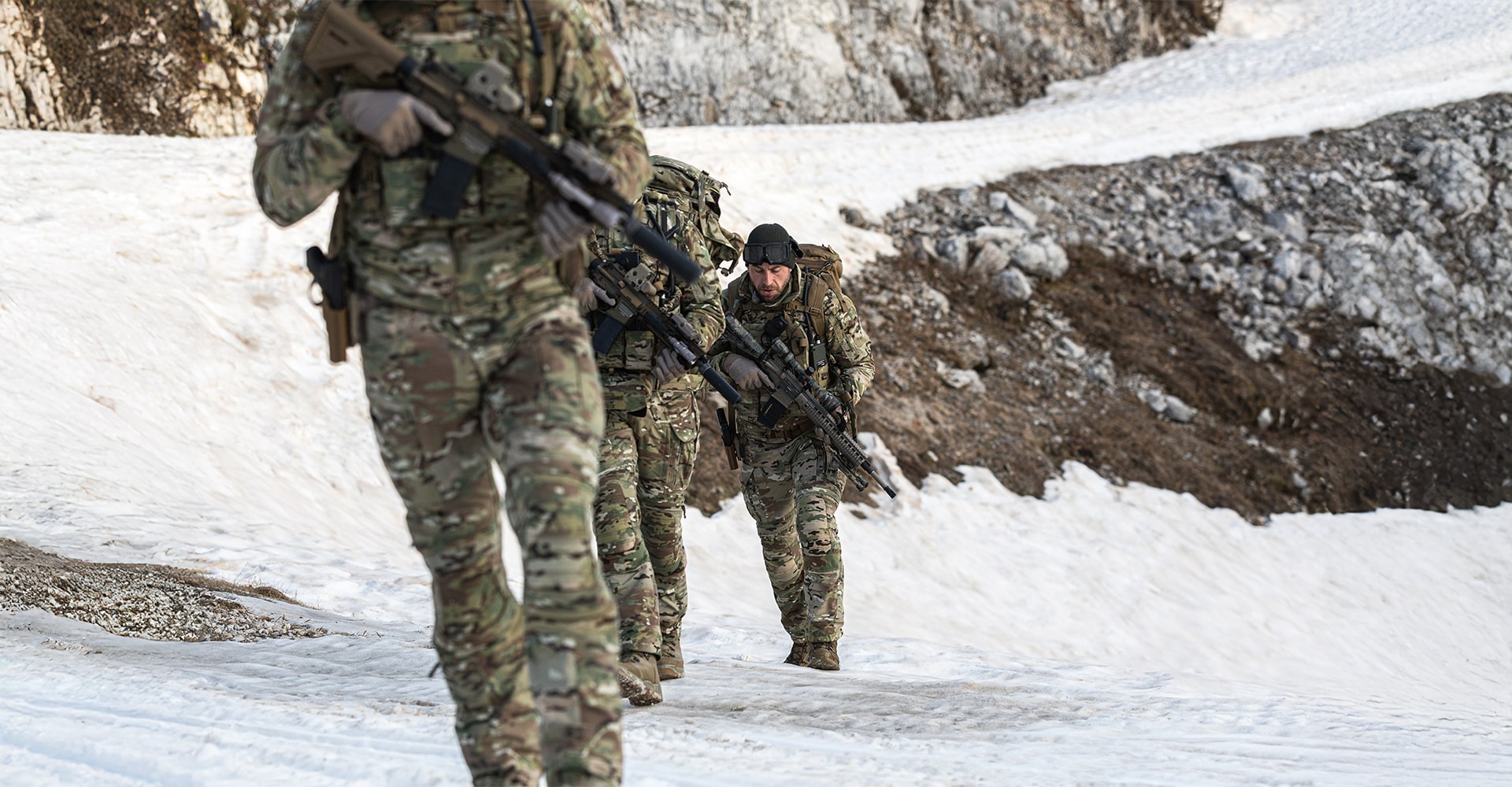 Operators trekking through snowy mountain terrain in full gear.
