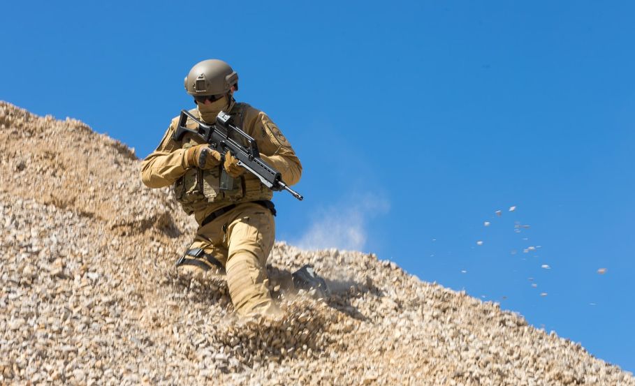 Operator sliding on one knee down rocky terrain in a tan military BDU, likely in a quarry setting. Are Your Combat Pants Built for Abuse? Here’s How to Tell