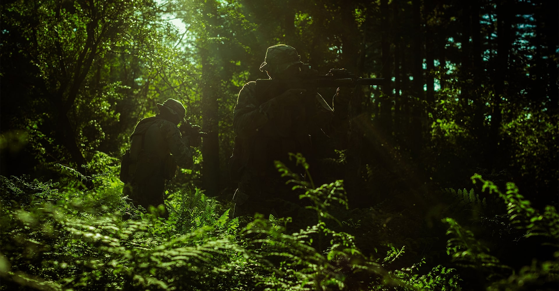 Two operators move through a dense, lush green jungle, with sunlight filtering through the trees behind them.