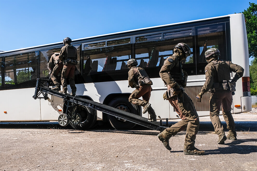 A group of soldiers, wearing mission-specific combat pants and knee pads, breaching into a bus.