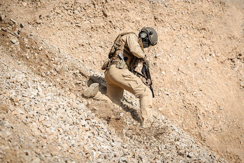 An operator in a tan uniform, sliding down on gravel, wearing knee pads.