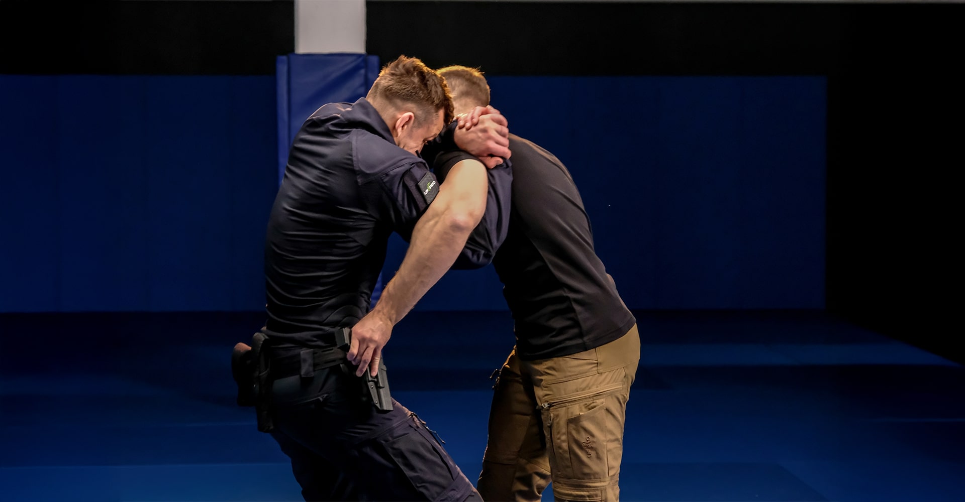 Two men demonstrating a front gun grab defense using an underhook and shoulder grip.