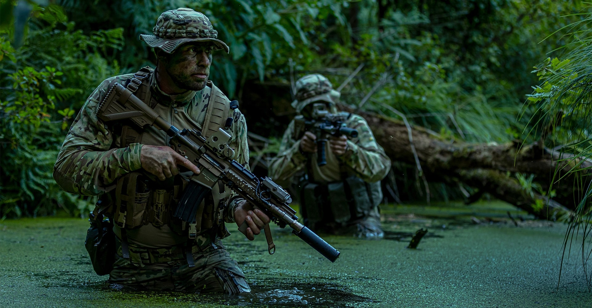 Operators wading through waist-deep swamp water in dense jungle terrain.