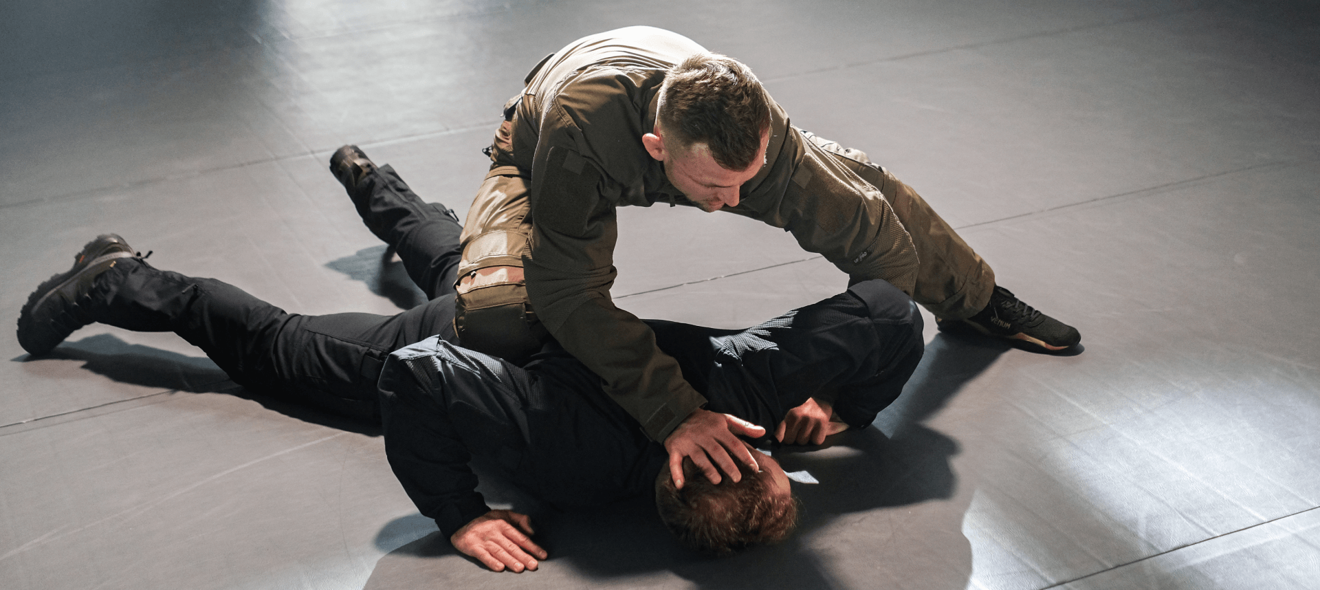 BJJ training exercise showing one person restraining another on the ground, using a knee-on-back technique to maintain control.