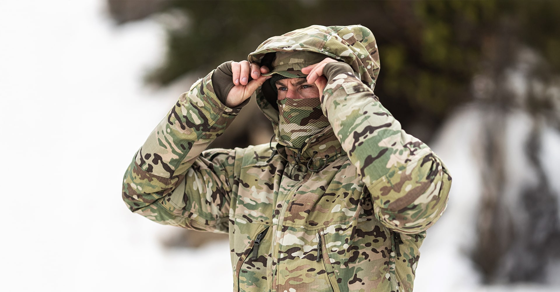 An operator adjusting his hood in a winter tactical outfit against a snowy backdrop.