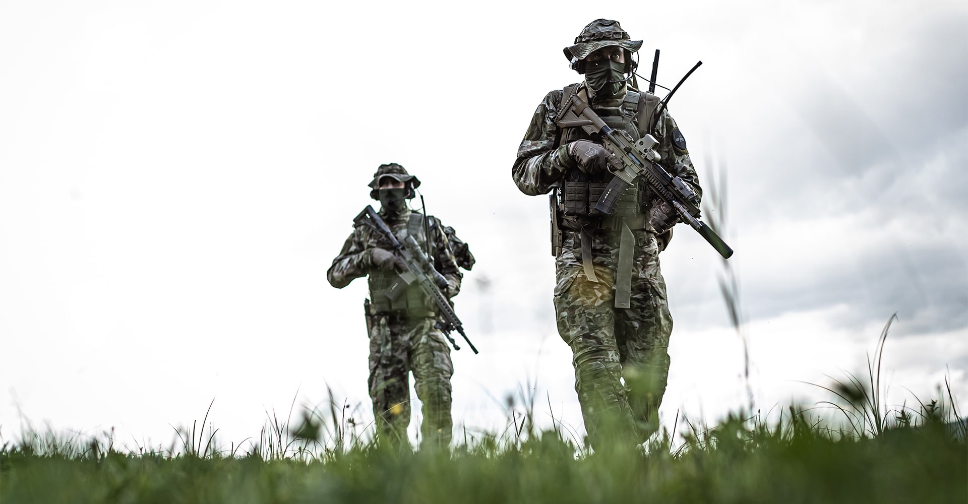 two operatiors in field both in tactical gear holding firearms