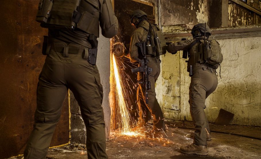 Military operators breaching a door using a power saw, with bright sparks flying in all directions. Is Your Flame-Retardant Garment Built for Movement—or Just Certification?