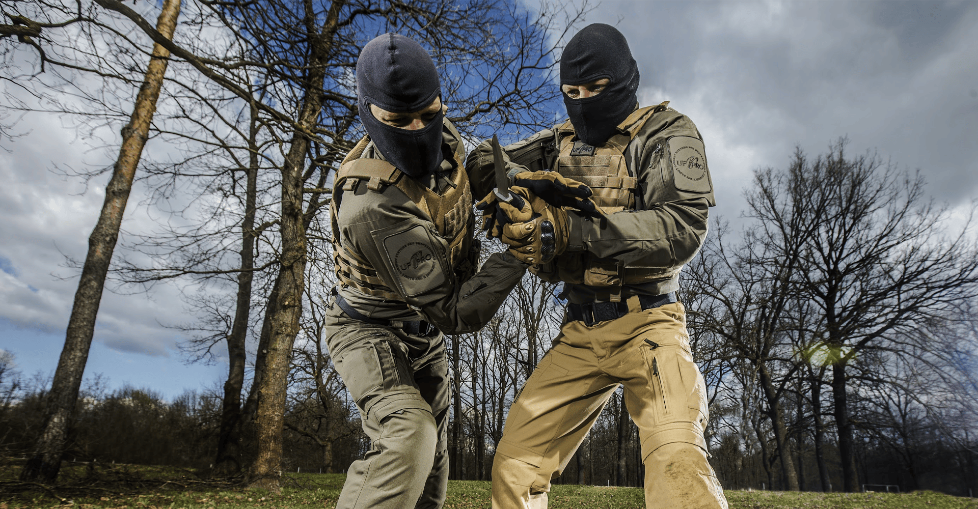 Two fully equipped operators wearing balaclavas engaged in a knife fight outdoors.