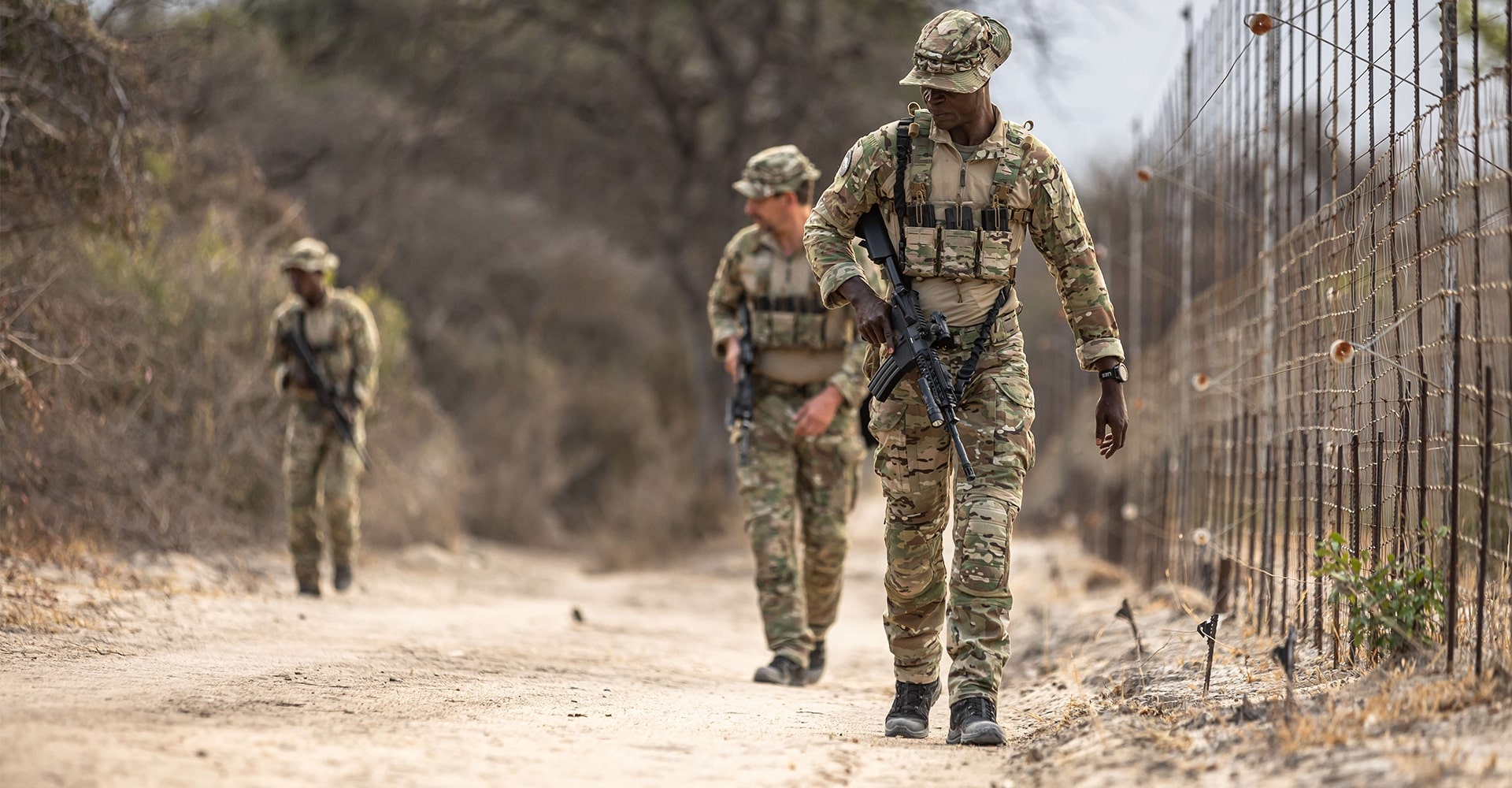 Three park rangers patrolling a fence in Africa's savanna, scanning for signs of potential illegal entries.