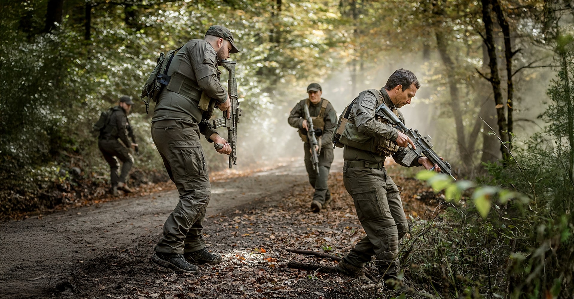 Utilizing tactical tracking techniques to follow a trail, four operators move along a muddy forest road in the early morning as fog gradually lifts, revealing their surroundings.