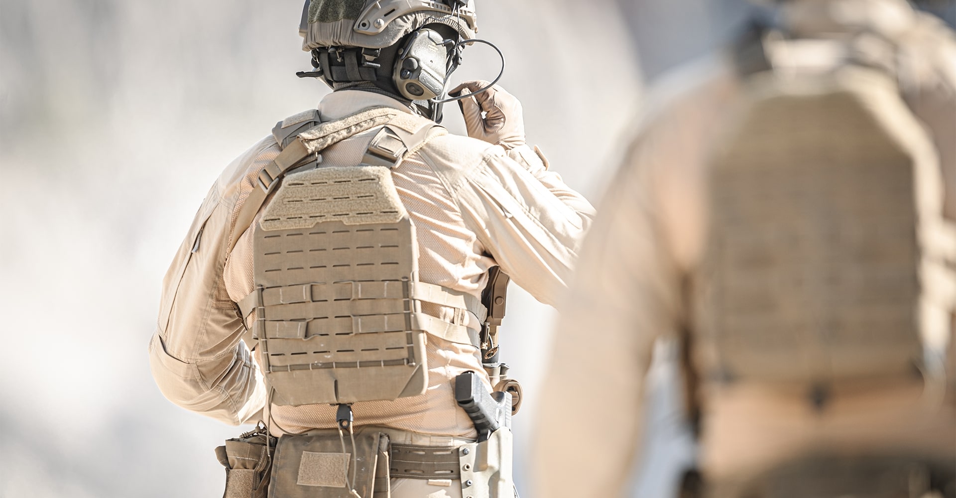 Close-up of two operators from behind wearing tan uniforms, indicating a hot and desert environment.