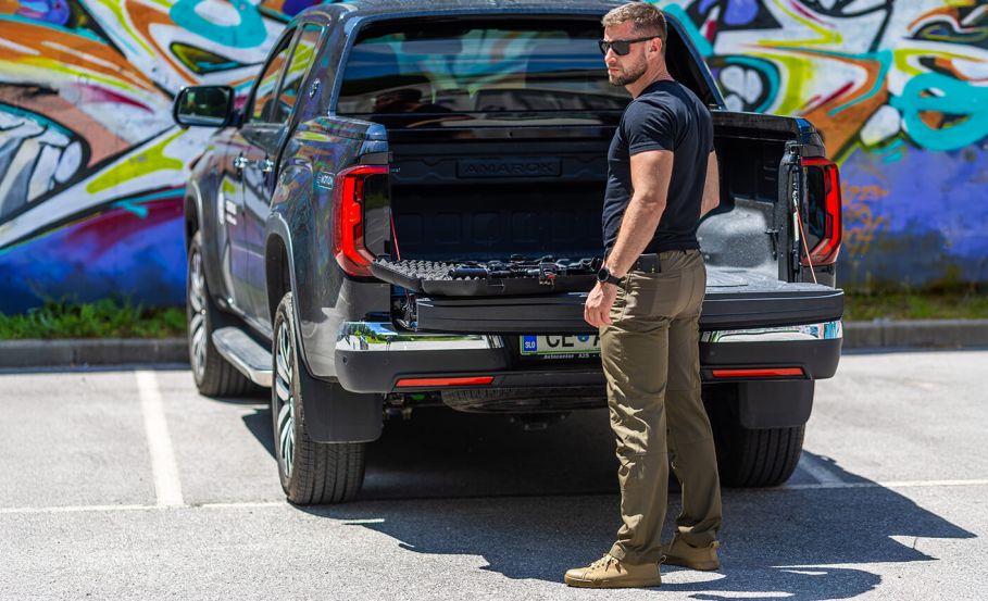 A man standing near an open truck bed in a parking lot, scanning his surroundings attentively.