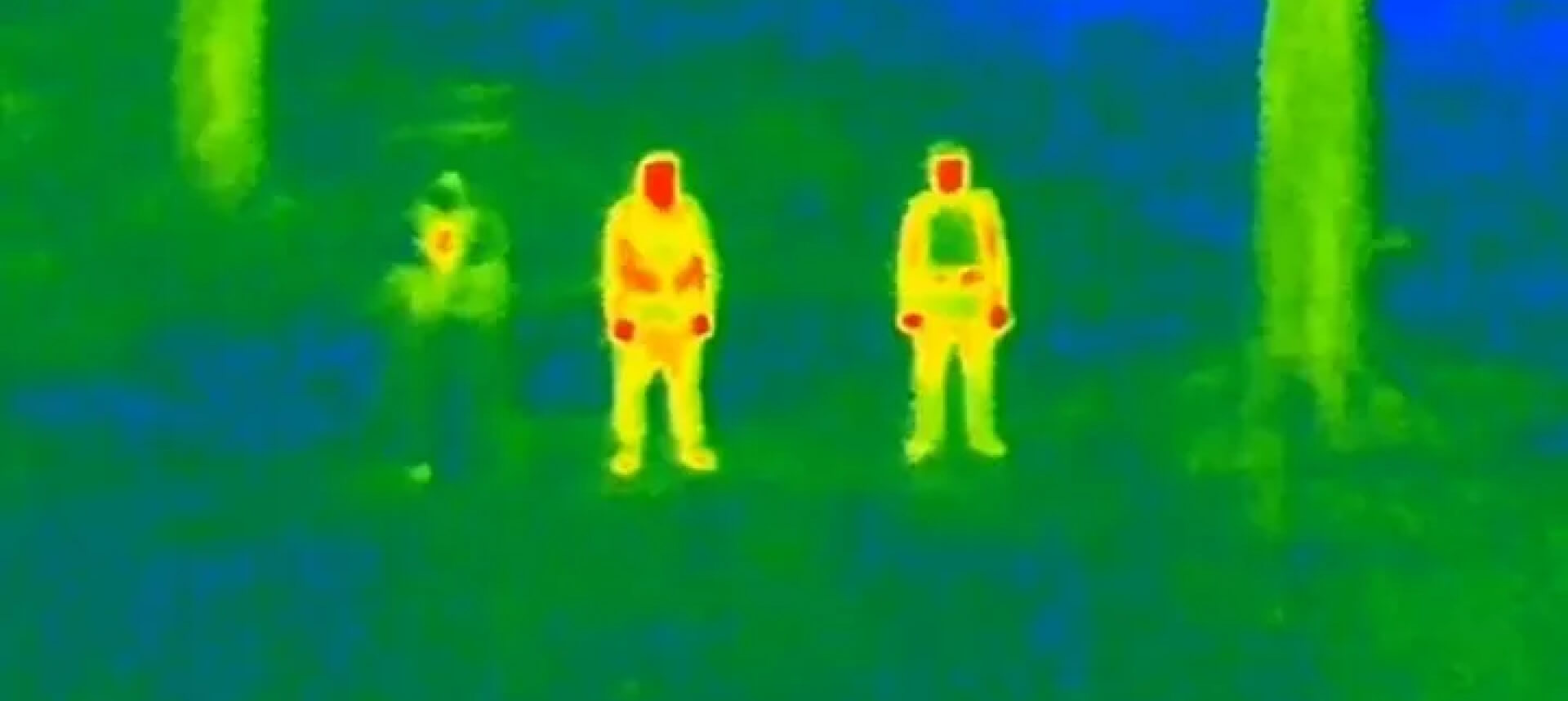 Thermal image of three figures emitting heat in bright tones, set against a cooler forest background.