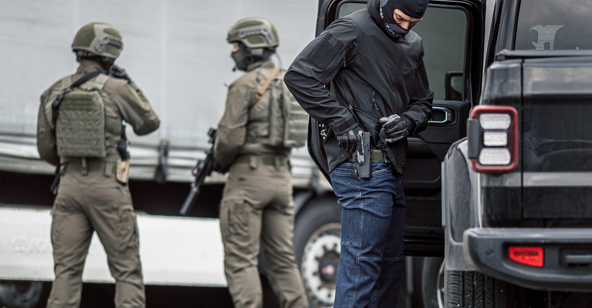 A law enforcement special forces operator preparing for a mission, with two other operators standing in the background.