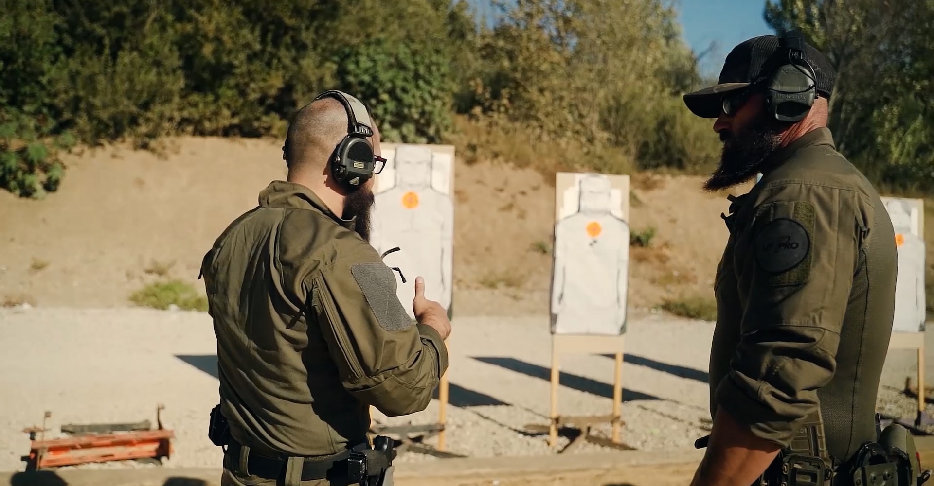 Two sports shooters on an outdoor range discussing and giving each other feedback.