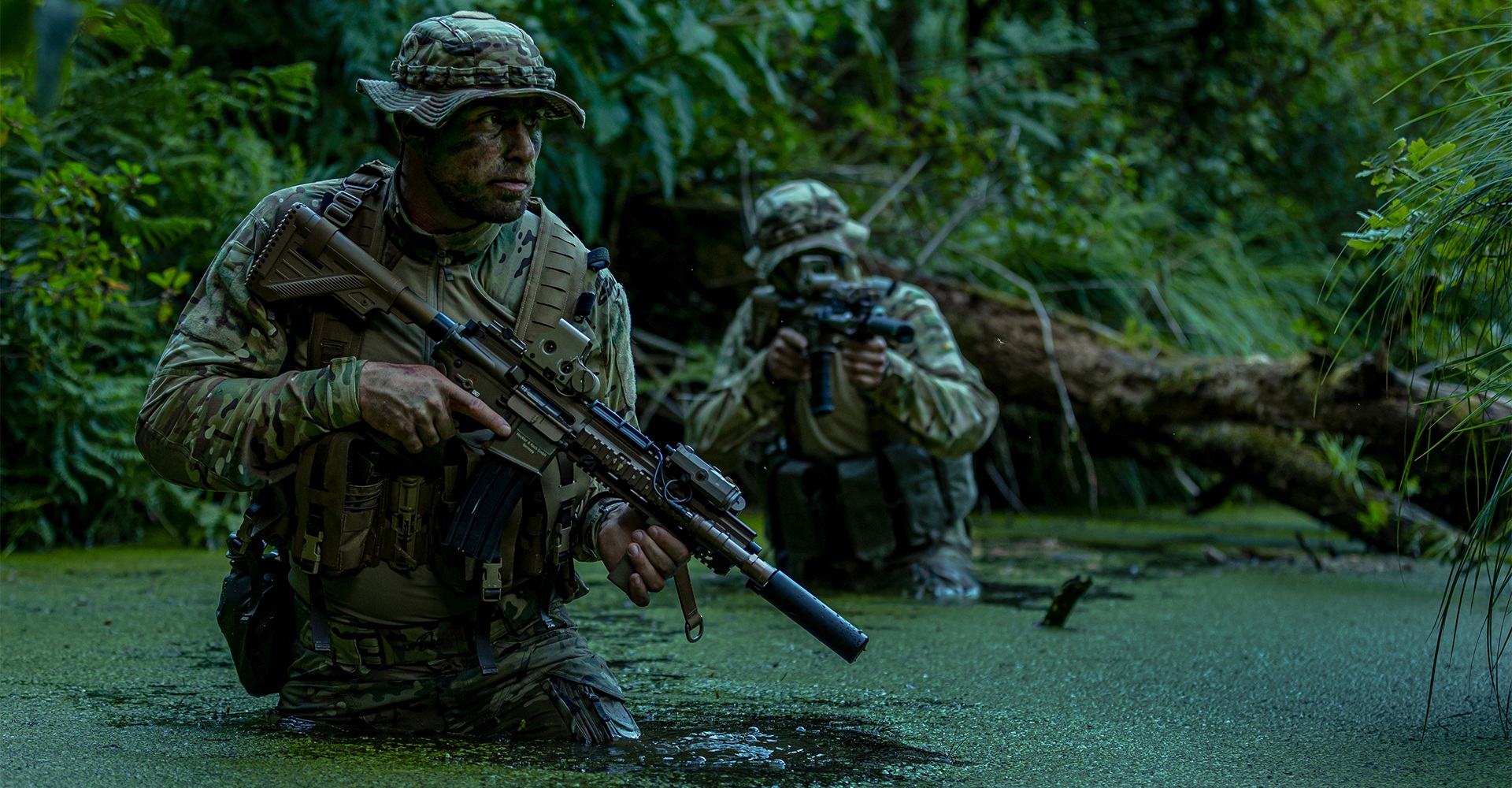 Two operators navigating a dense jungle swamp, fully equipped for the mission.