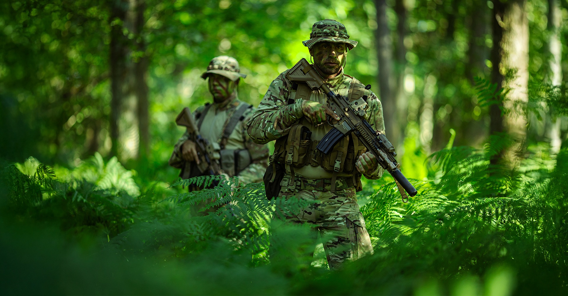 Two operators moving through dense jungle terrain, fully prepared for jungle warfare.