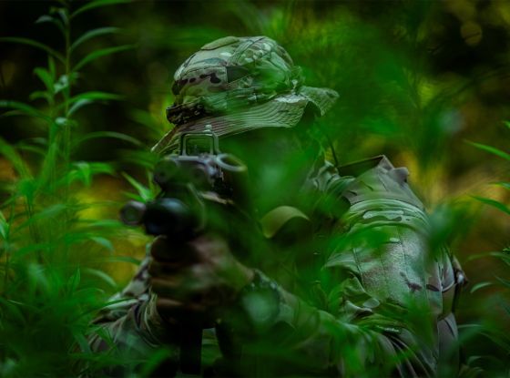 Operator in dense jungle foliage, aiming at a target with his firearm.