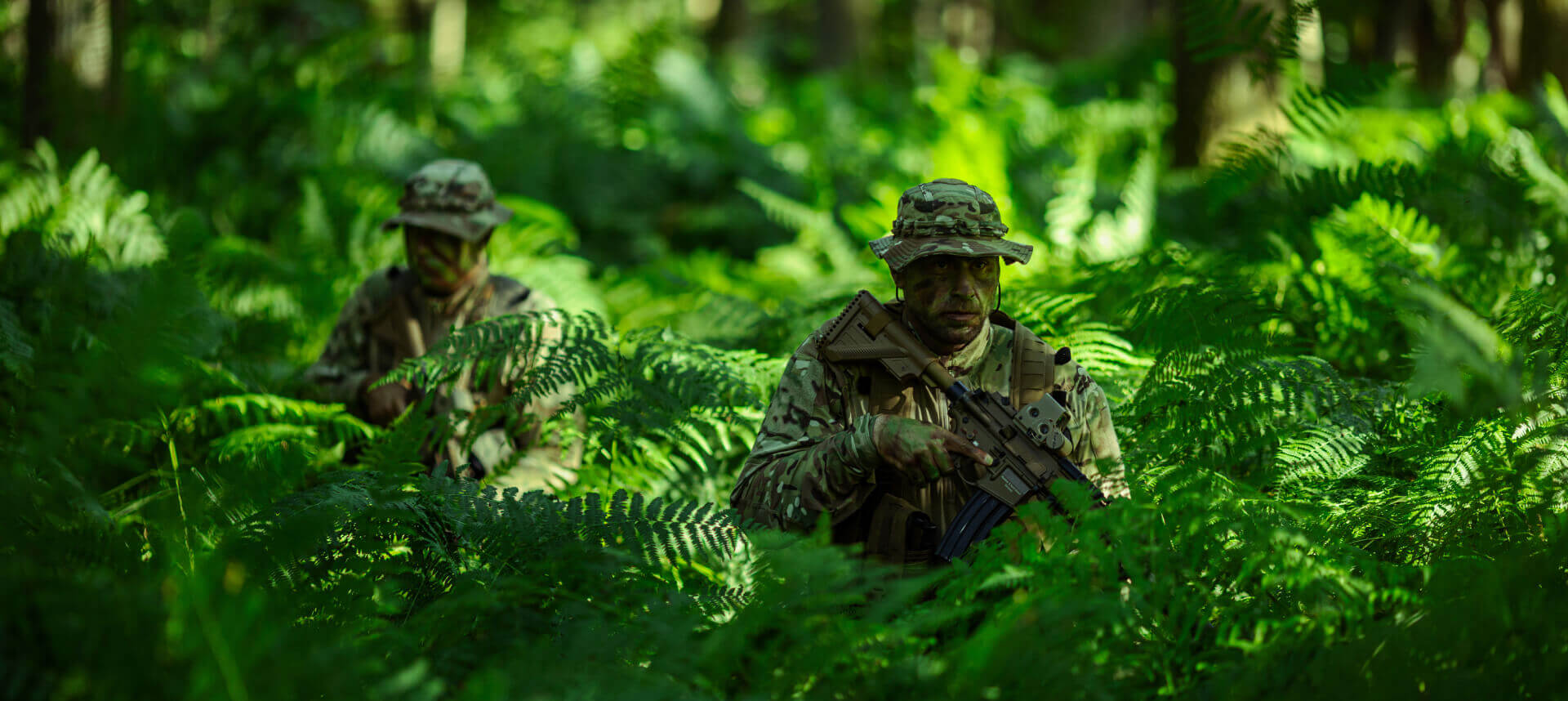 Two soldiers in dense tropical foliage, demonstrating the effectiveness of camouflage in varying light and shadow conditions.