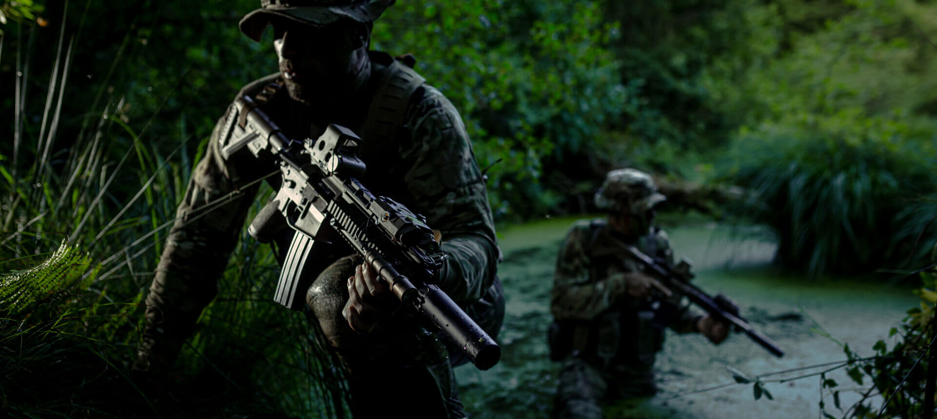 Soldiers moving through swampy terrain, emphasizing camouflage adaptability to water reflections and dense vegetation.