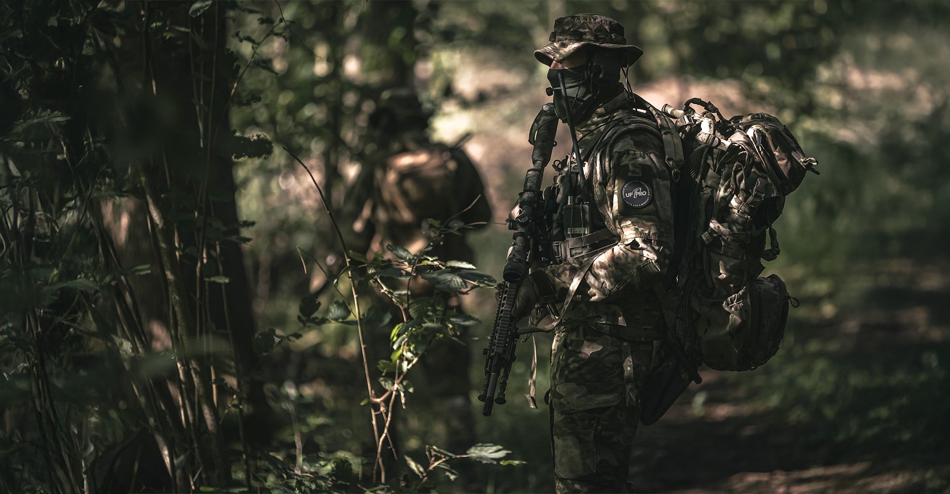 Two operators in camouflage tactical clothing attempting to blend into the surrounding forest.