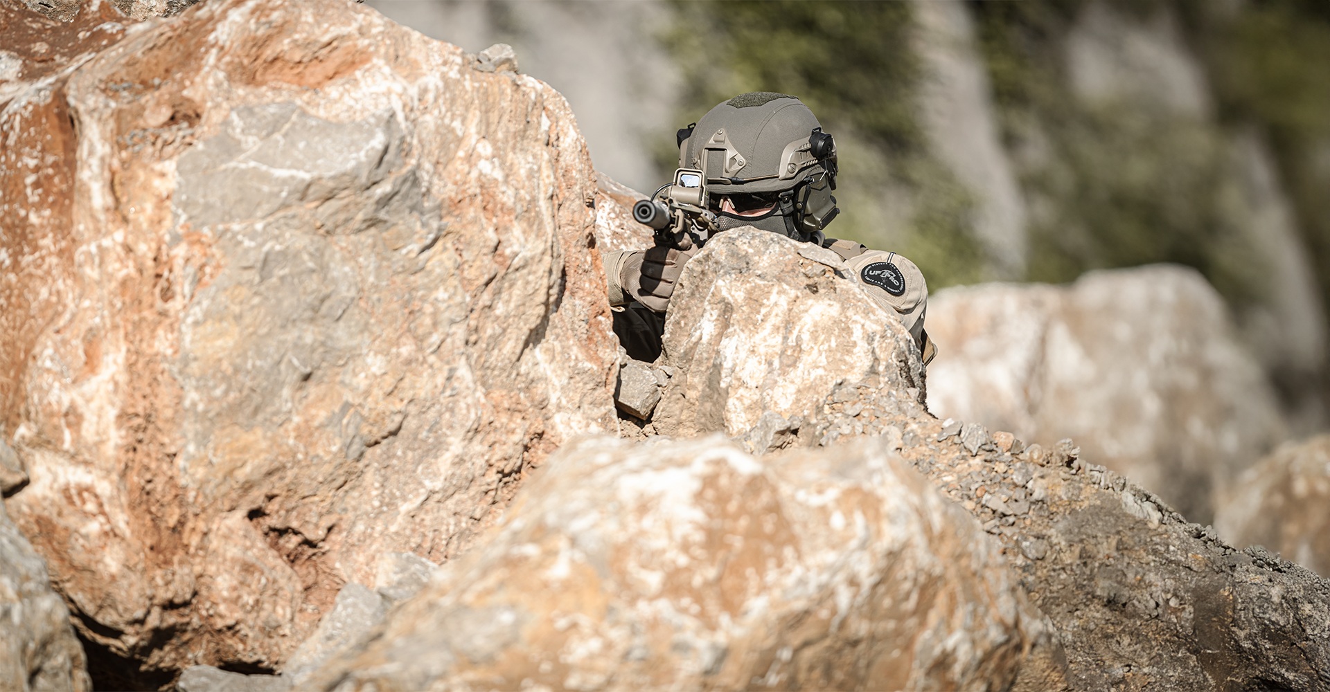 Operator taking cover behind a rock, using it to conceal his position while leveraging its heat to blend his thermal signature.