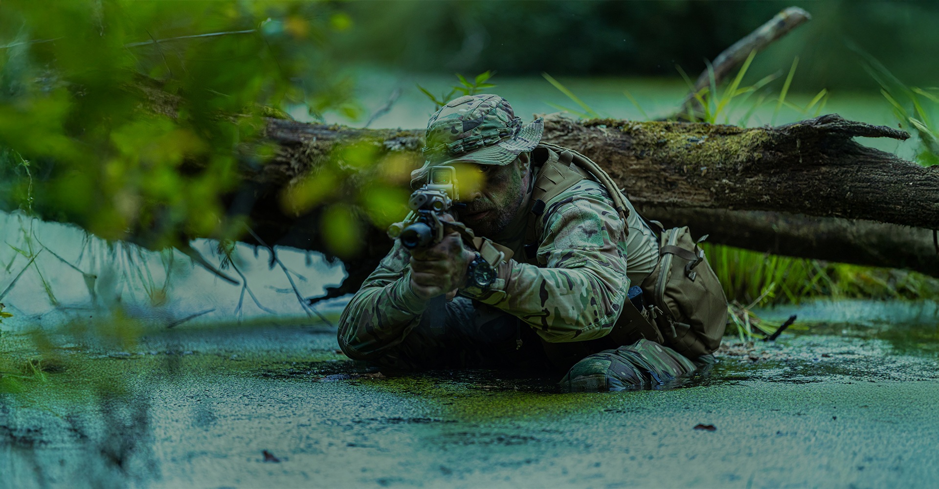 Operator submerged in muddy, swampy water, carefully aiming his firearm while staying concealed beneath the surface.