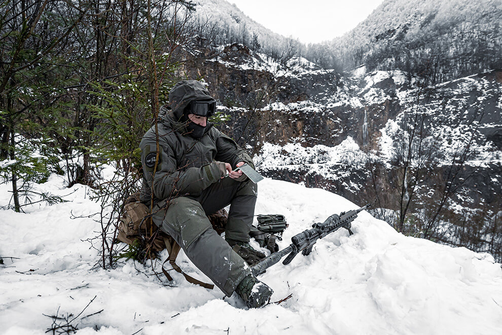 A tactical operator sitting down in the snow and reading notes