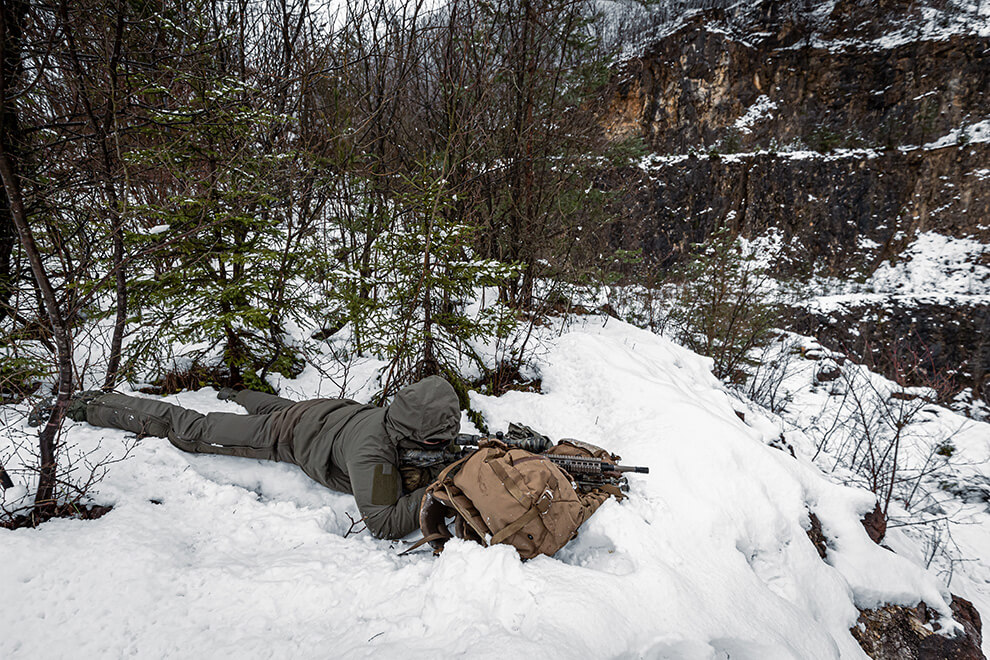 Tactical operator lying down in the snow and aiming
