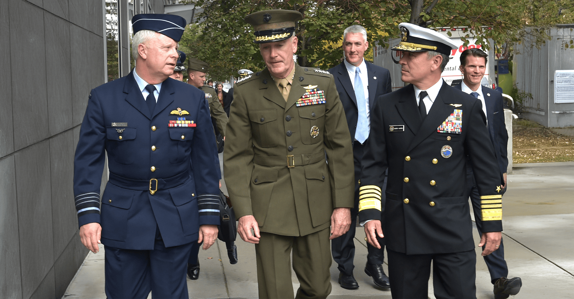 Three high-ranking officers in service dress uniforms walking down a city street, engaged in conversation.