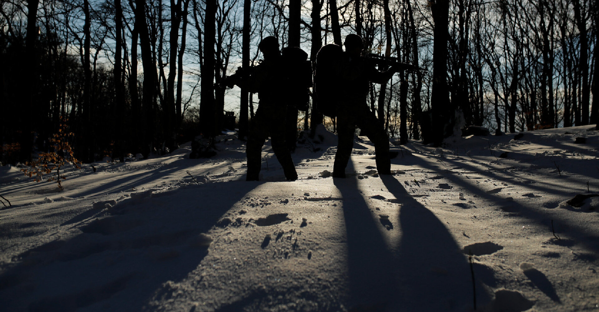 Two operators casting shadows in a snowy forest as sunlight filters through the trees.