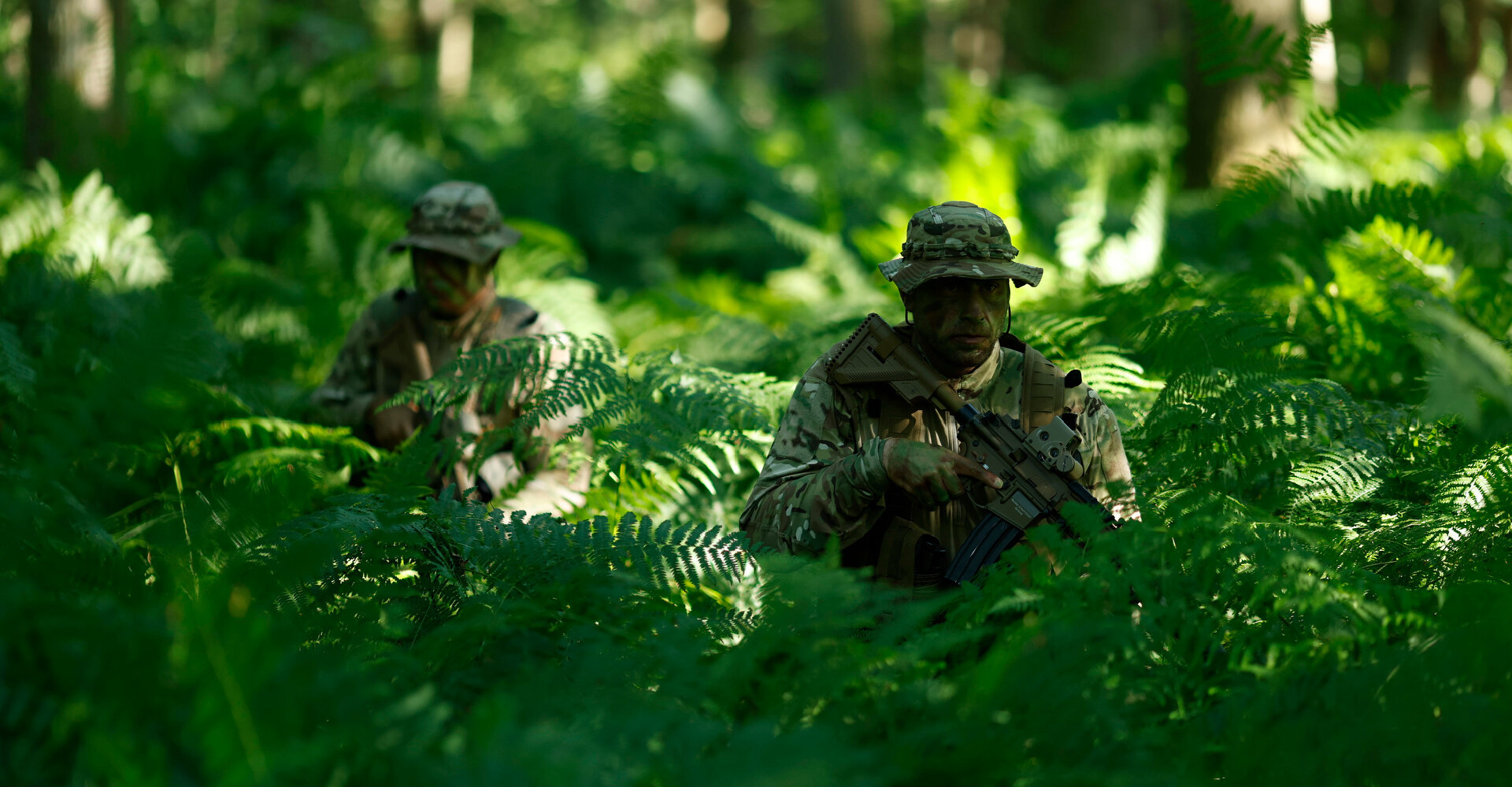 Two operators in camouflage uniforms navigating through dense jungle vegetation.