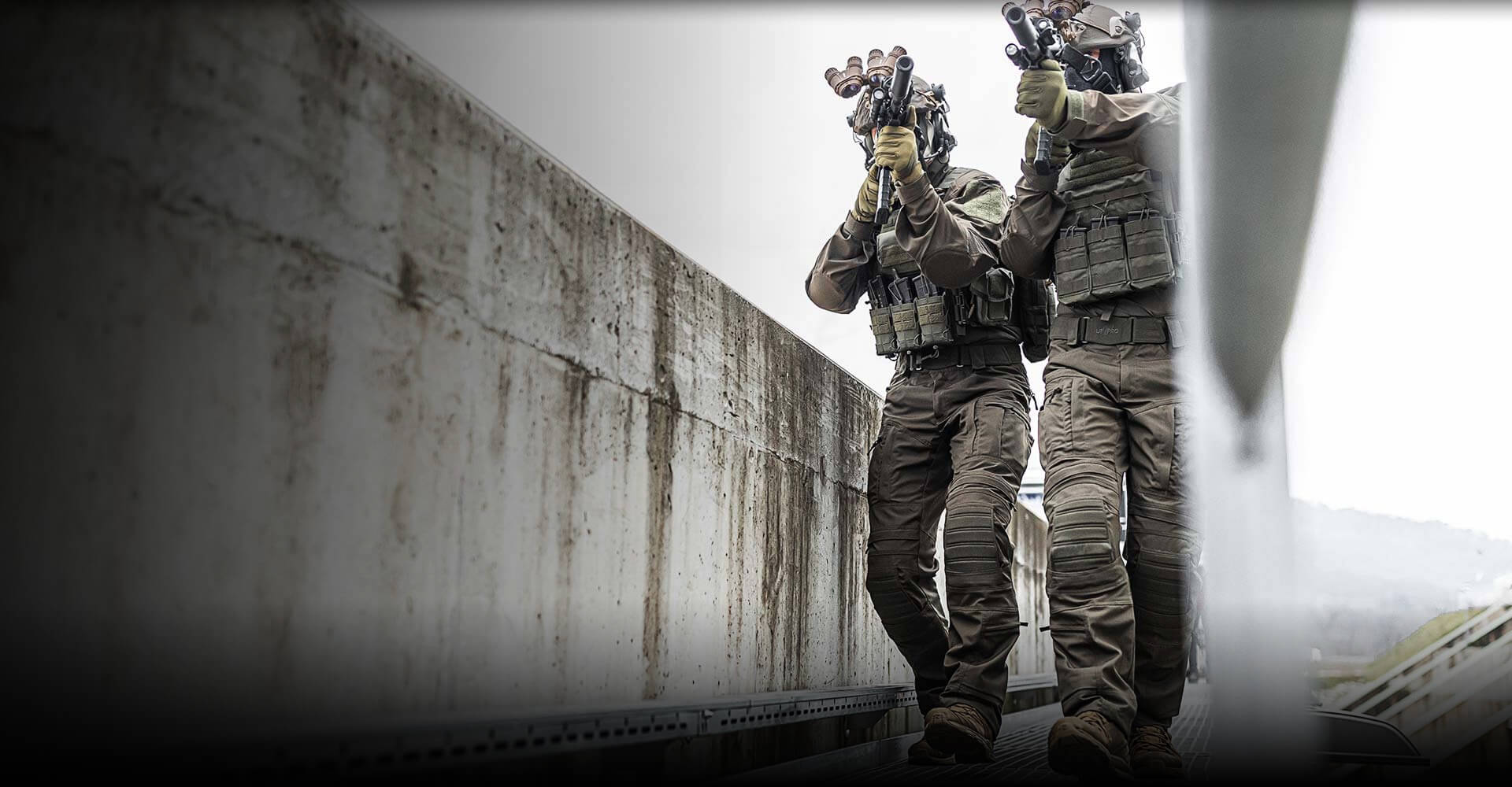 Two tactical operators on a bridge wearing a Striker XT Gen.3 BDU and carrying a rifle.