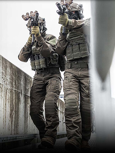 Two tactical operators on a bridge wearing a Striker XT Gen.3 BDU and carrying a rifle.