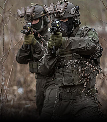 Two tactical operators standing in the underbrush wearing Striker XT Gen.3 Combat Shirt and carrying a rifle.