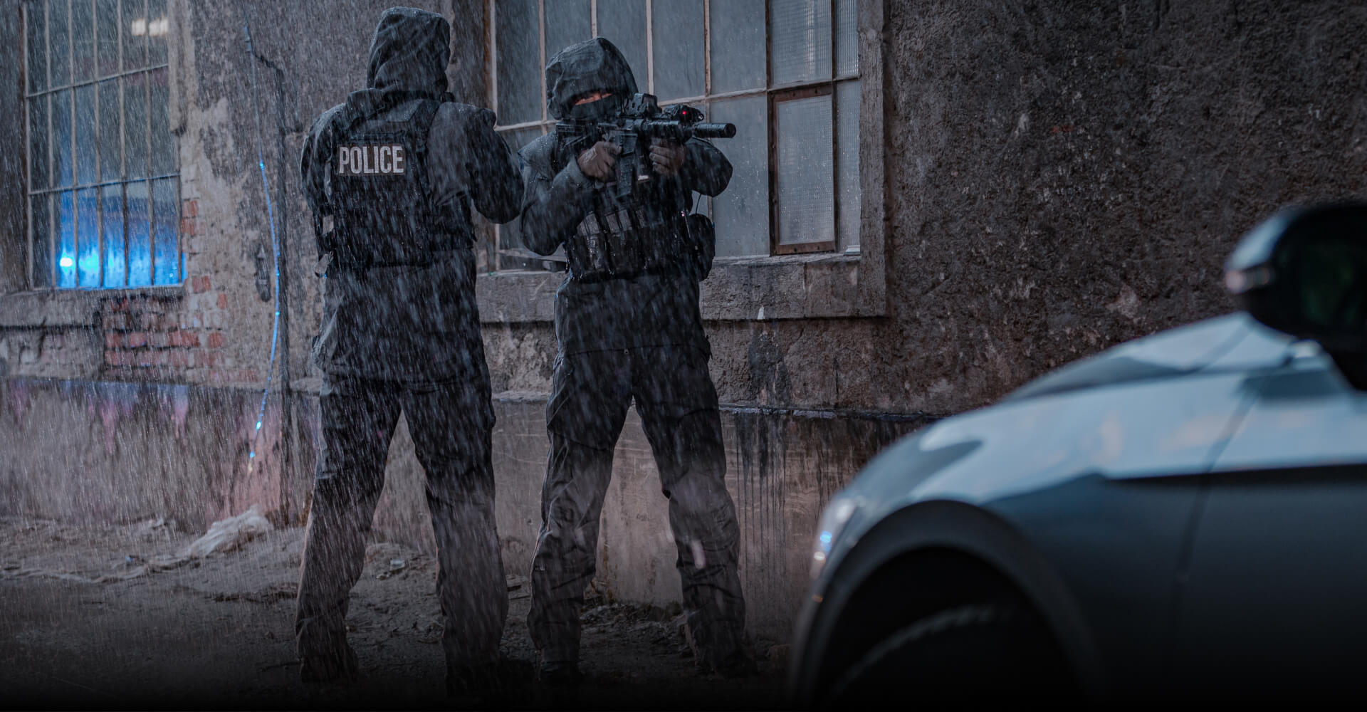 UNDERSTANDING WEATHER EXTREMES Two police officers in rain suits securing a perimeter in a severe downpour in front of an abandoned industrial building.
